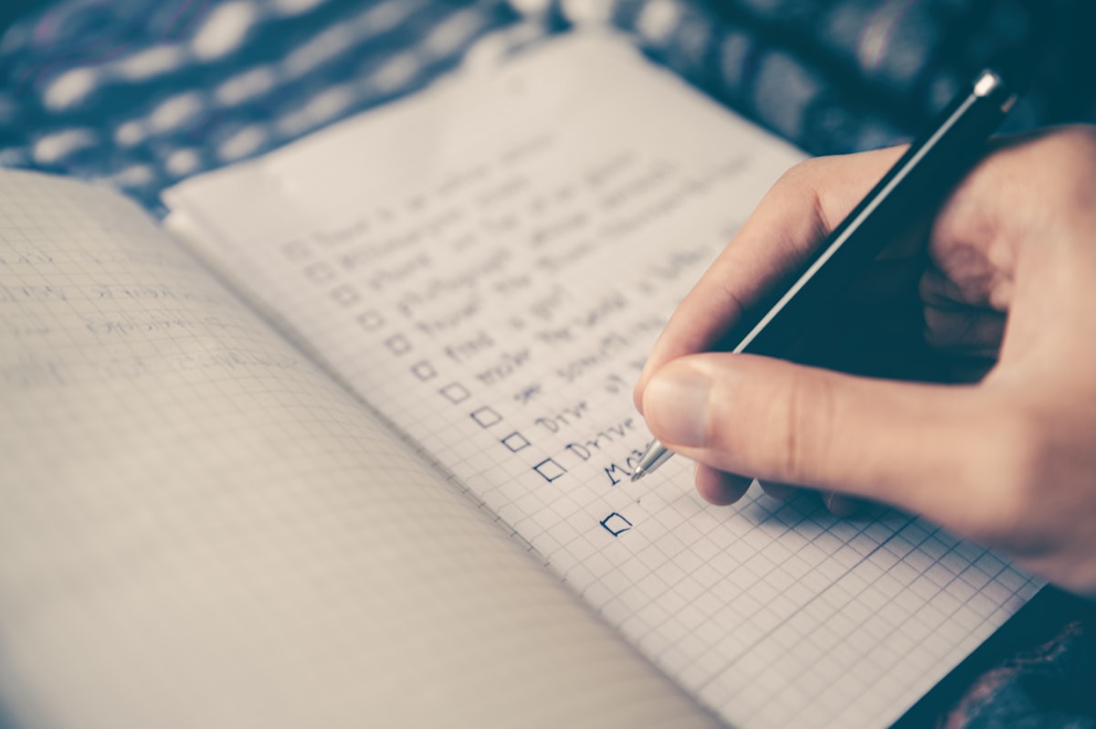 A hand writing a list in an open notebook.